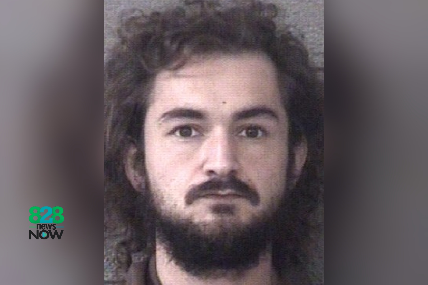 Mugshot-style head-and-shoulders photo of a man with long dark hair and a full beard, neutral backdrop, 828 News Now logo in the bottom left.
