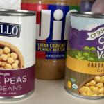 Three canned pantry items: Delallo chickpeas (garbanzo beans) on the left, Jif Extra Crunchy Peanut Butter in the center, and Green Valley Organics garbanzo beans on the right.