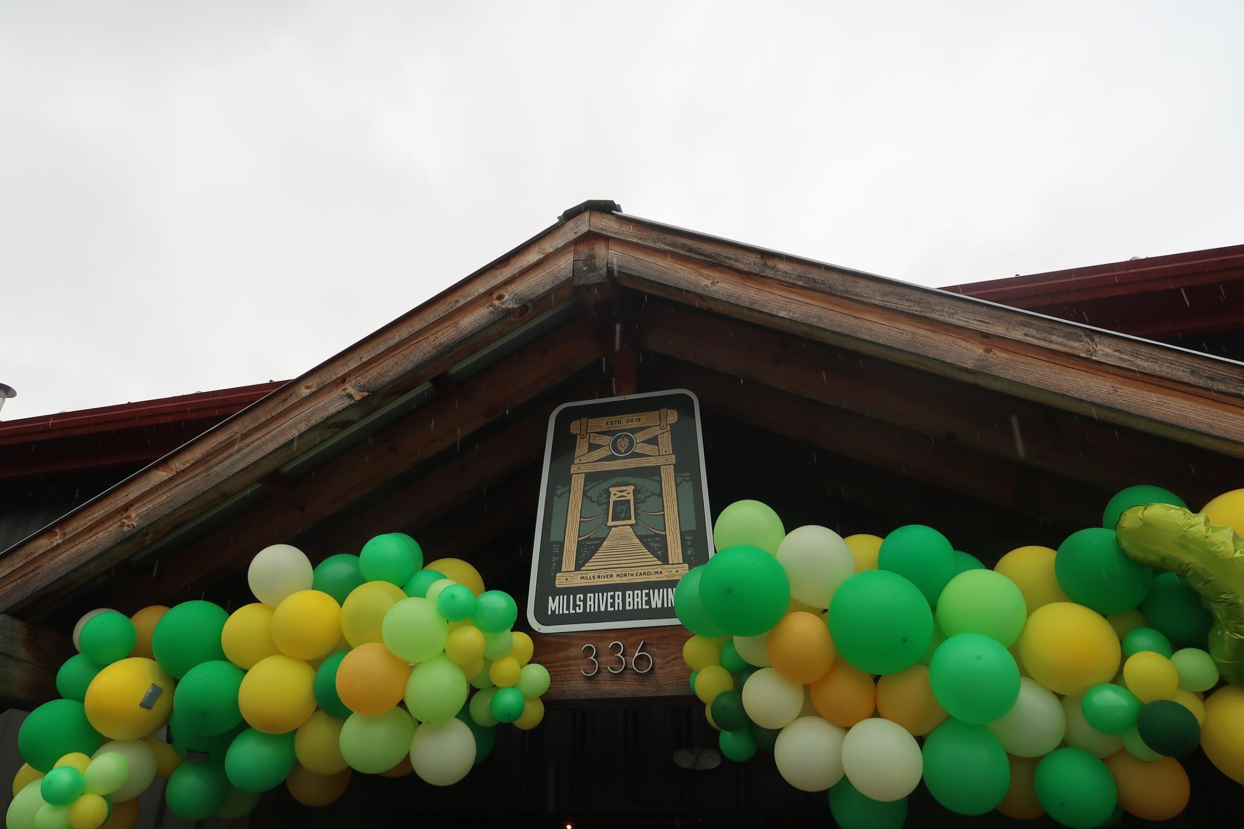 Entrance of Mills River Brewing with green, yellow, and white balloons around the wooden beams and a sign reading Mills River Brewing (est. 2015).