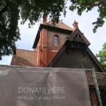 Brick church with red-tiled roof visible through surrounding trees; foreground banner reads “Donate Here” for All Souls Cathedral rebuild.