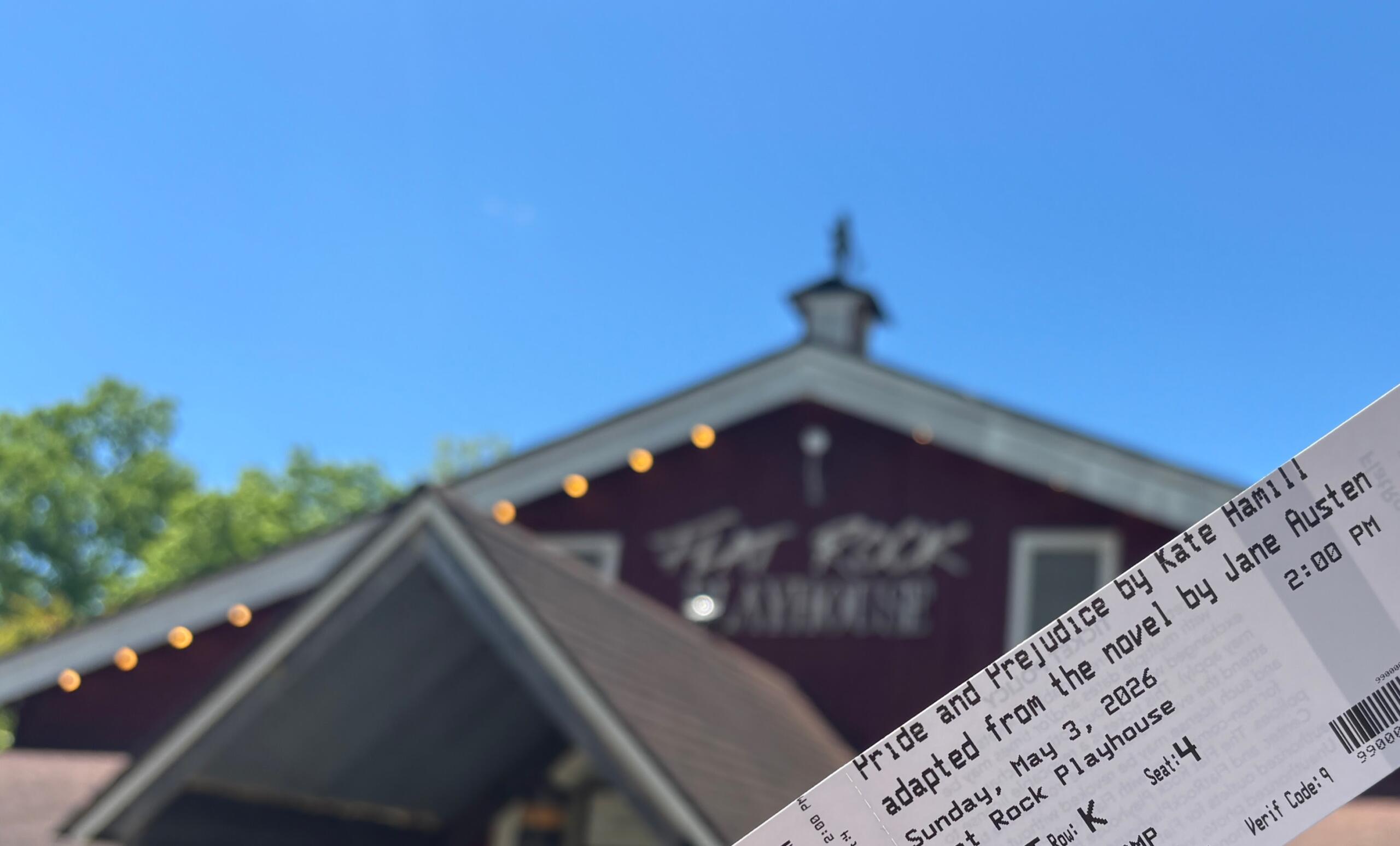 Close-up of a printed event ticket in the foreground with a blurred building and blue sky in the background.