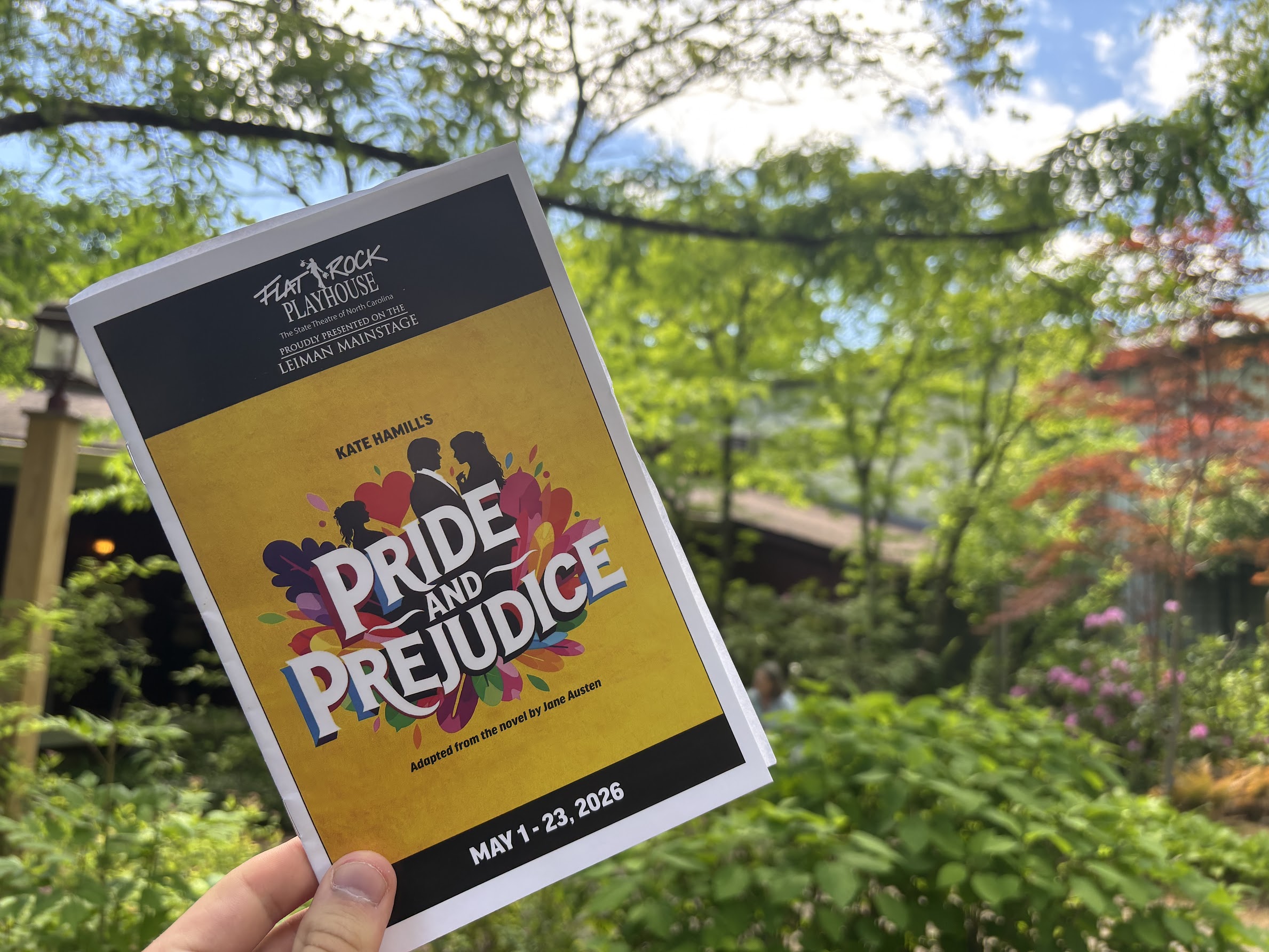 Outdoor poster for Pride and Prejudice by Jane Austen, held by a hand against a leafy background.