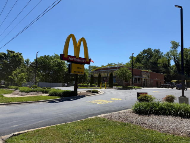 McDonald's sign with golden arches and red panel, restaurant building in background on a sunny day.