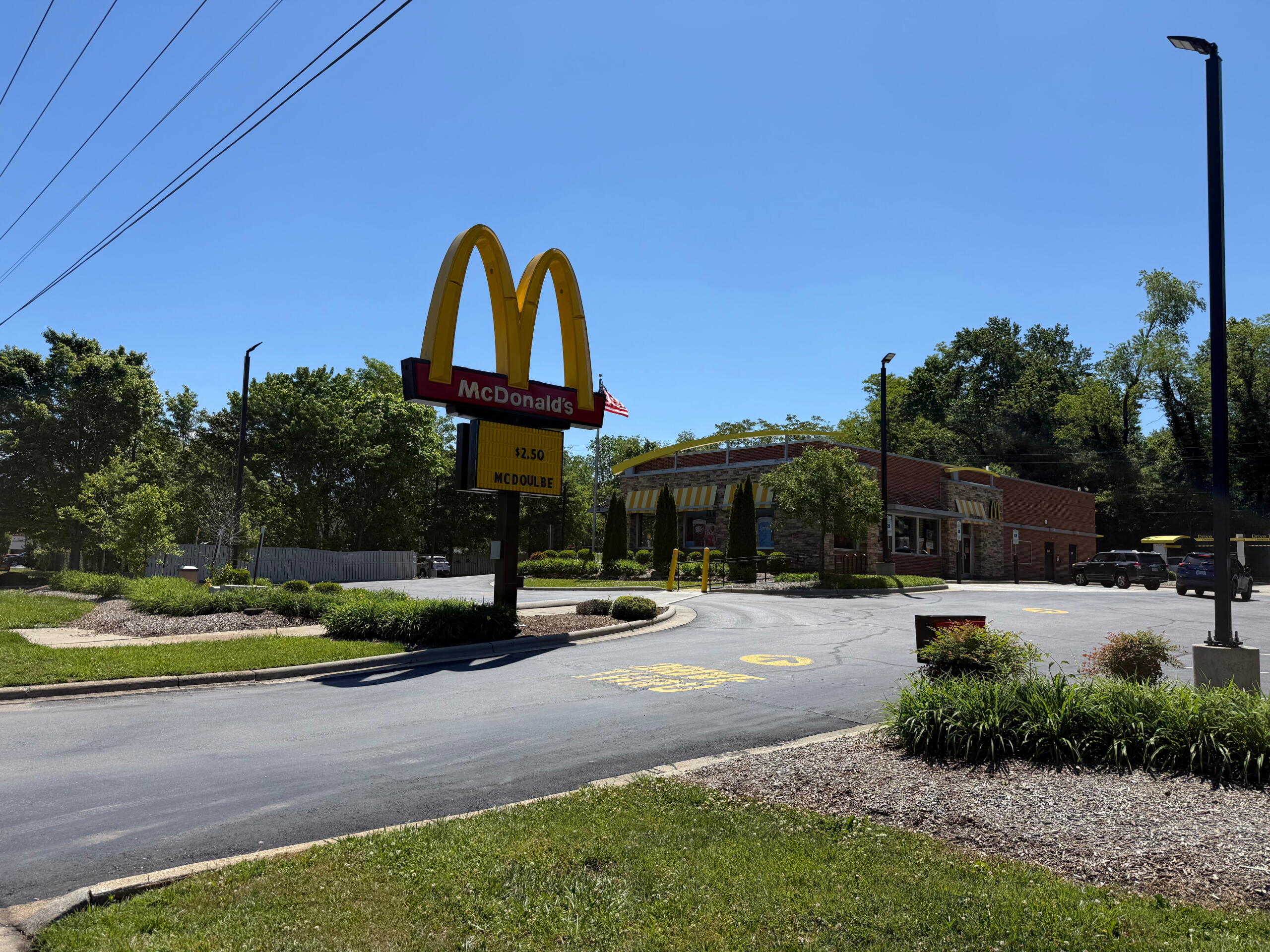 McDonald's sign with golden arches and red panel, restaurant building in background on a sunny day.