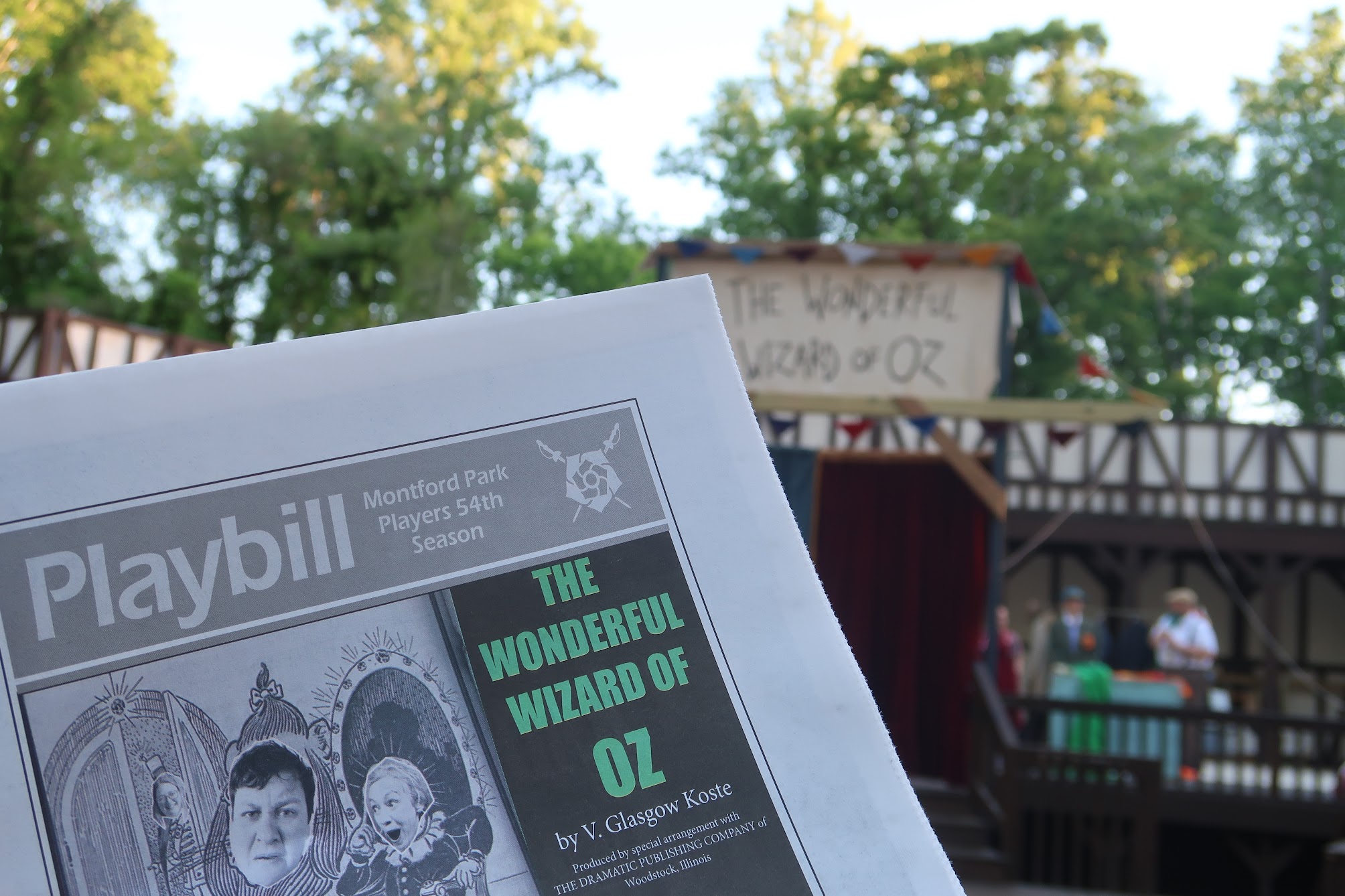Close-up of a Playbill program for The Wonderful Wizard of Oz being held outdoors, with trees in the background.