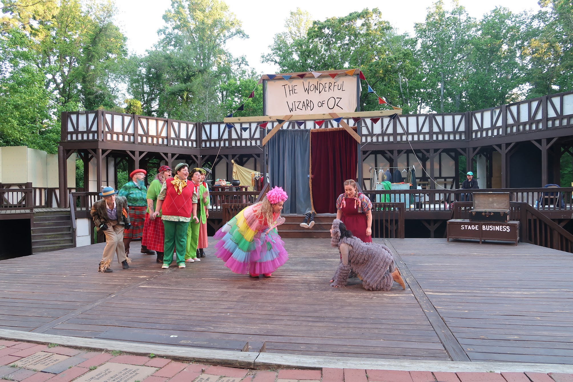 Stage performance of The Wonderful Wizard of Oz with colorful costumes and performers on a wooden outdoor set.