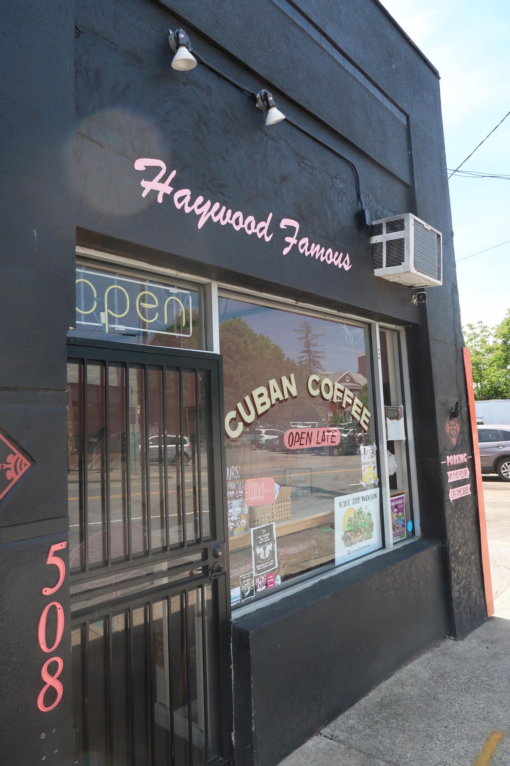 Dark storefront with a pink cursive sign reading 'Haywood Famous' above a large window showing 'Cuban Coffee' and an 'Open' sign.