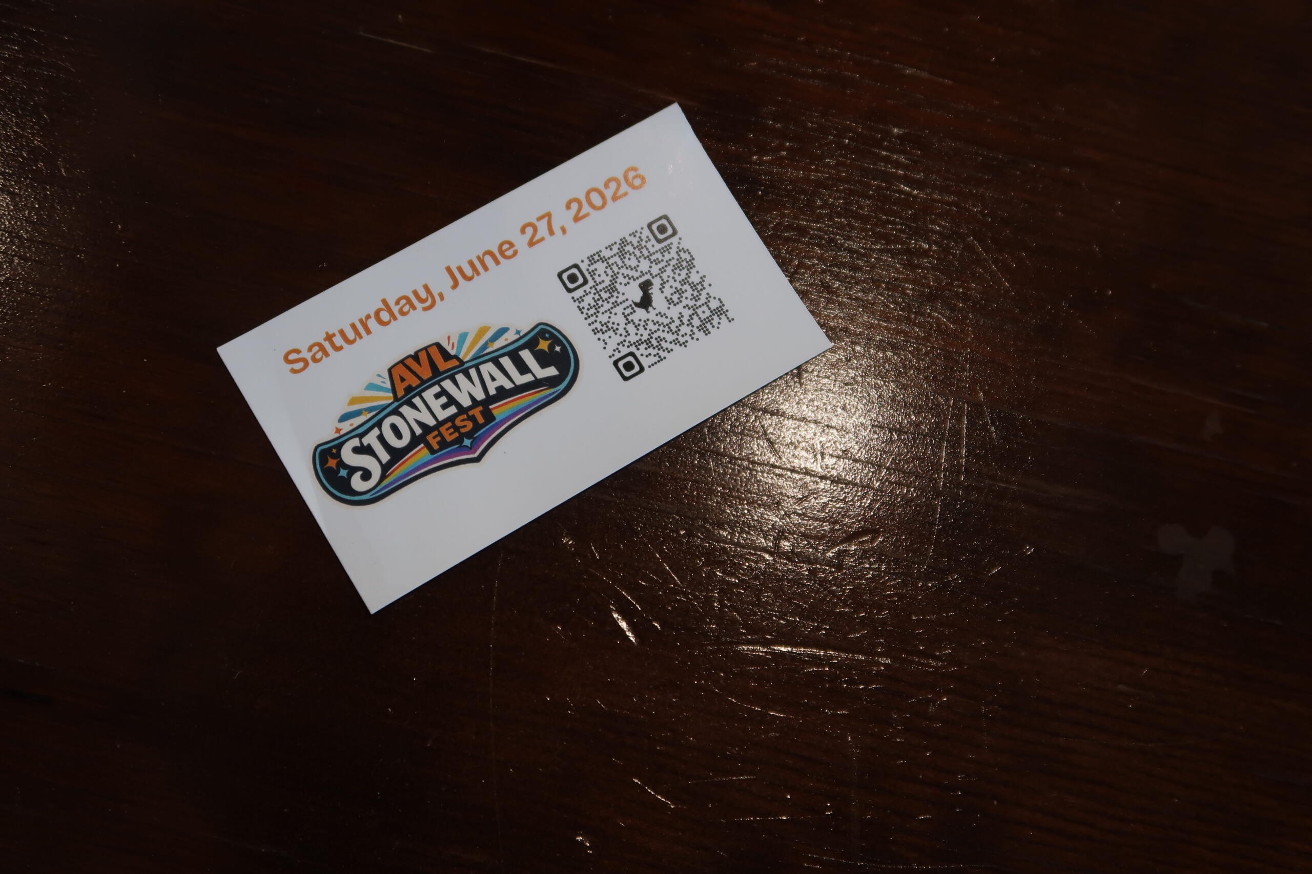 Event ticket on a dark wooden surface showing 'Saturday, June 27, 2026', a colorful festival logo, and a QR code.