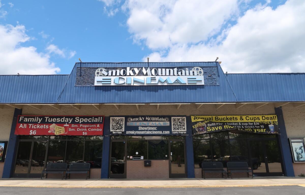 Smoky Mountain Cinema storefront with blue metal awning and promotional banners outside the entrance, under a blue sky.