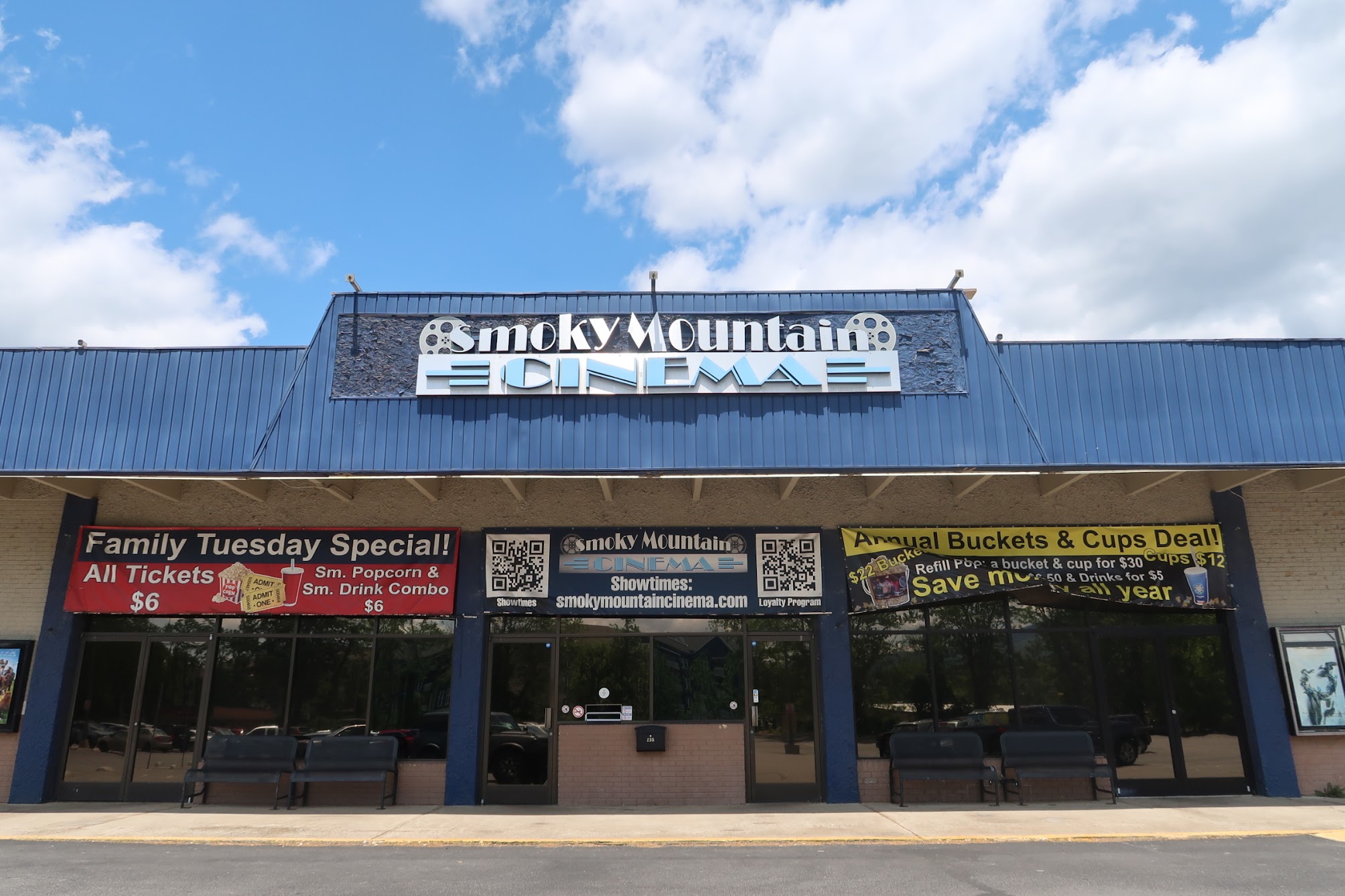Smoky Mountain Cinema storefront with blue metal awning and promotional banners outside the entrance, under a blue sky.