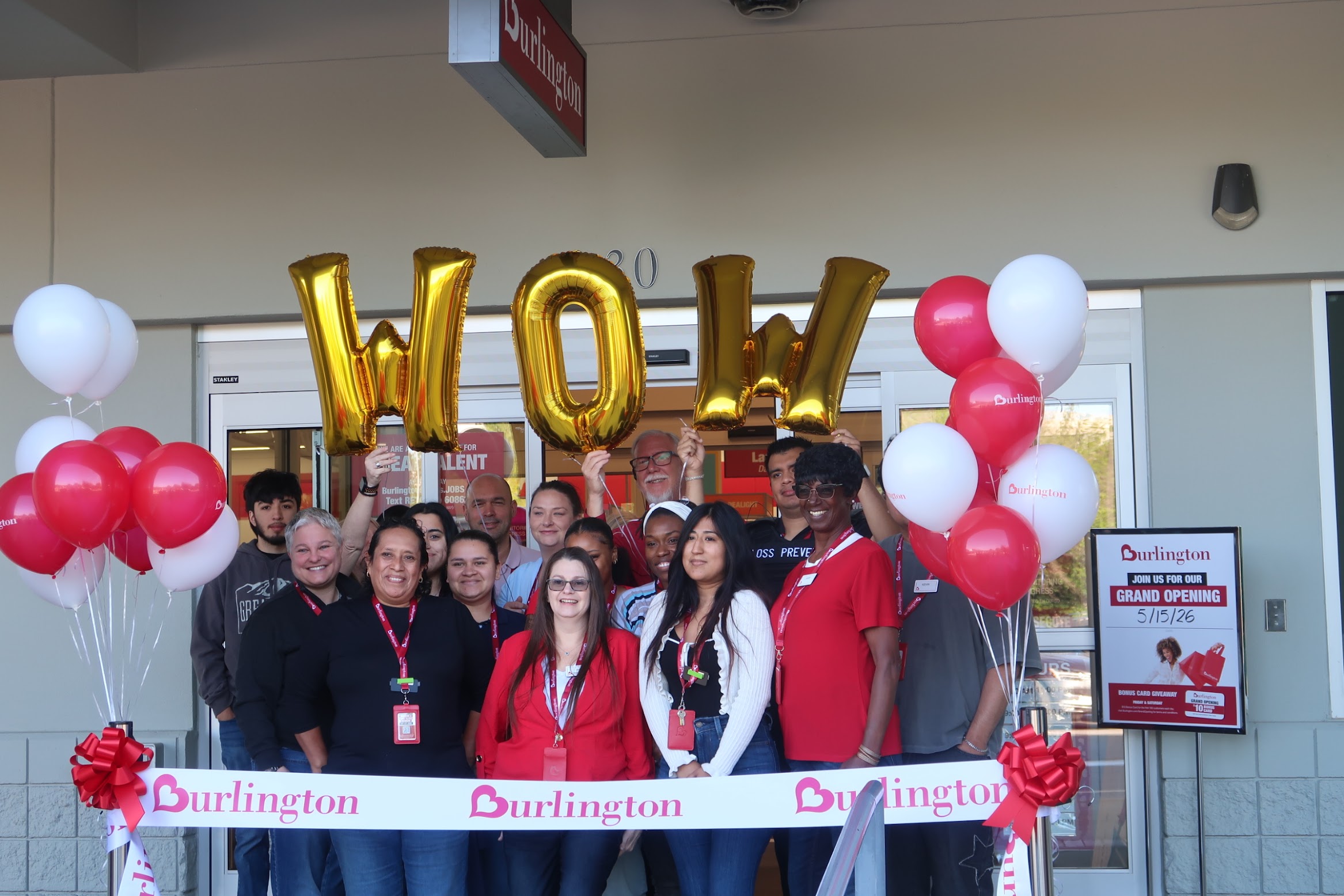 Crowd of people at a Burlington grand opening, holding gold letter balloons with red and white balloons and a branded ribbon.