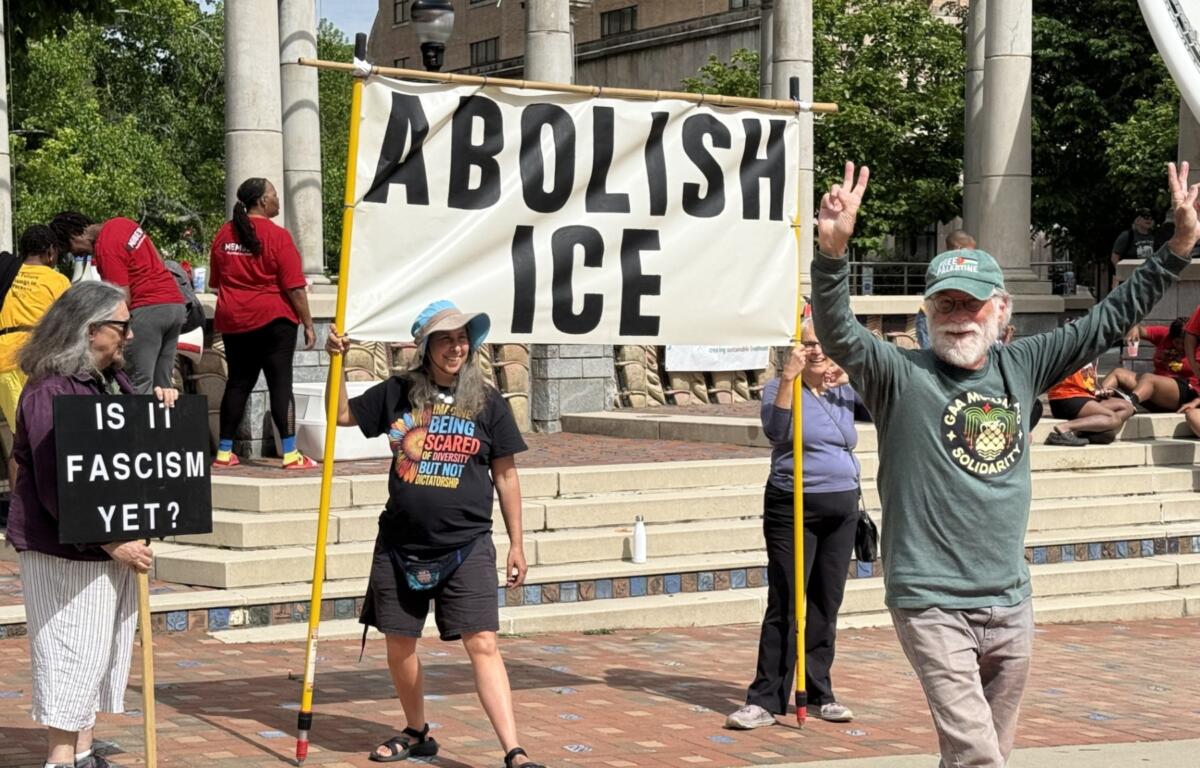 Group of protesters on steps holding a large 'ABOLISH ICE' banner and a sign reading 'Is it fascism yet?'.