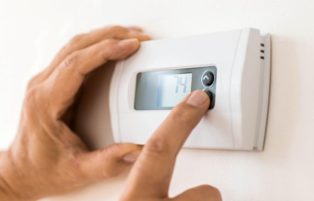 Person adjusting a wall-mounted thermostat with a digital display in a home setting.