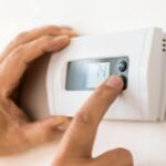 Person adjusting a wall-mounted thermostat with a digital display in a home setting.