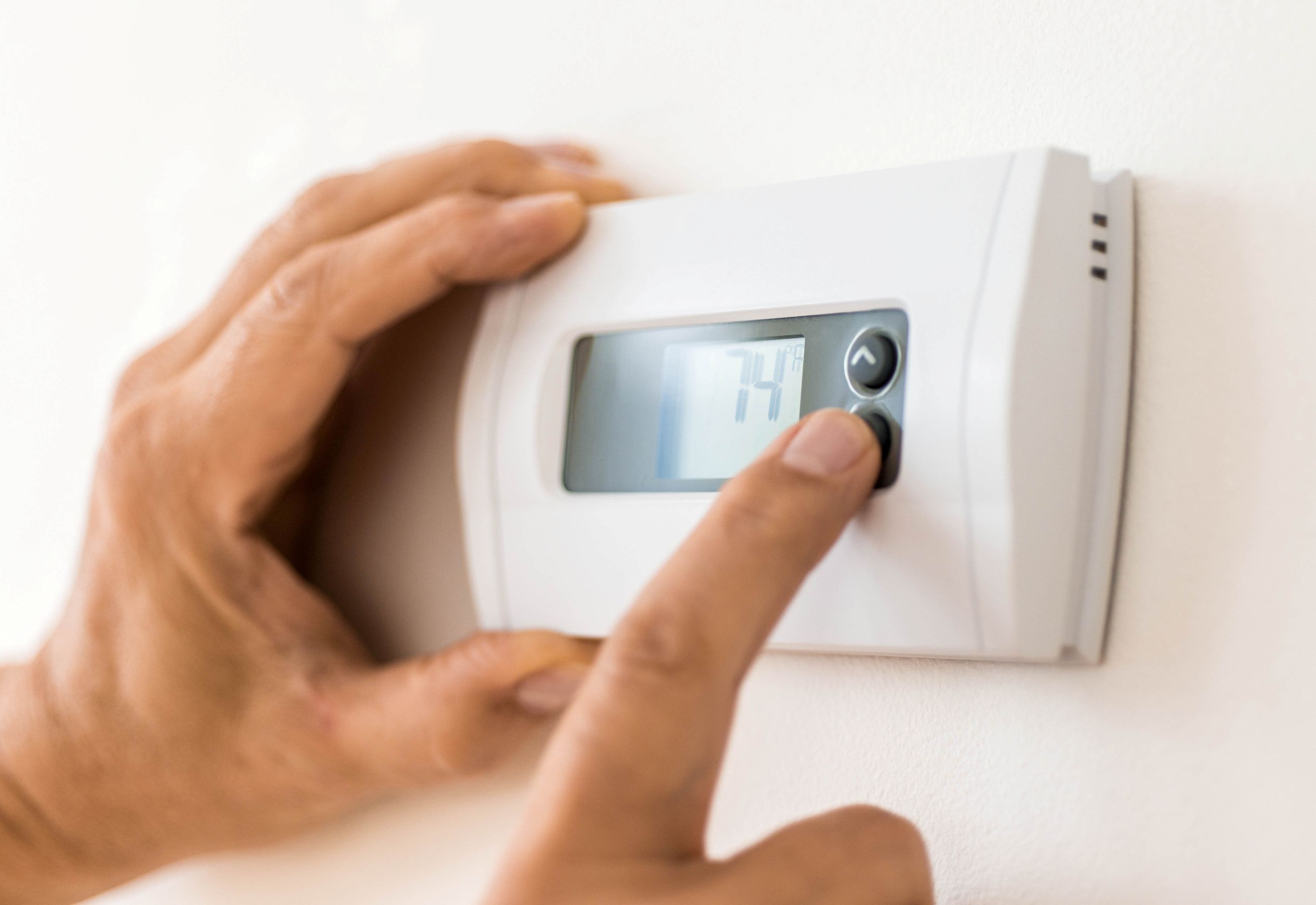 Person adjusting a wall-mounted thermostat with a digital display in a home setting.