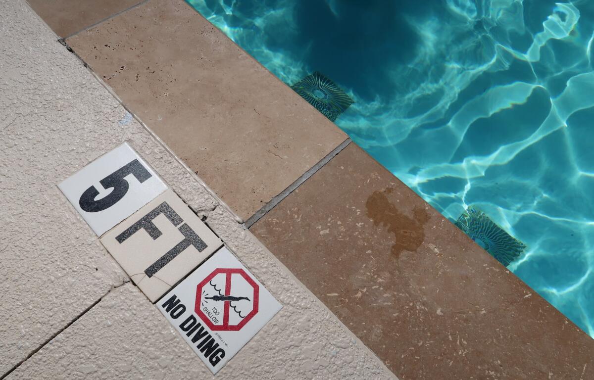 Pool deck with warning signs near the water edge, including 'No diving' and 'Too shallow' messages.