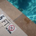 Pool deck with warning signs near the water edge, including 'No diving' and 'Too shallow' messages.