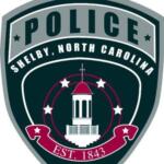 Shield-shaped police emblem for Shelby, North Carolina, with a central white courthouse tower, stars, and EST. 1843 text