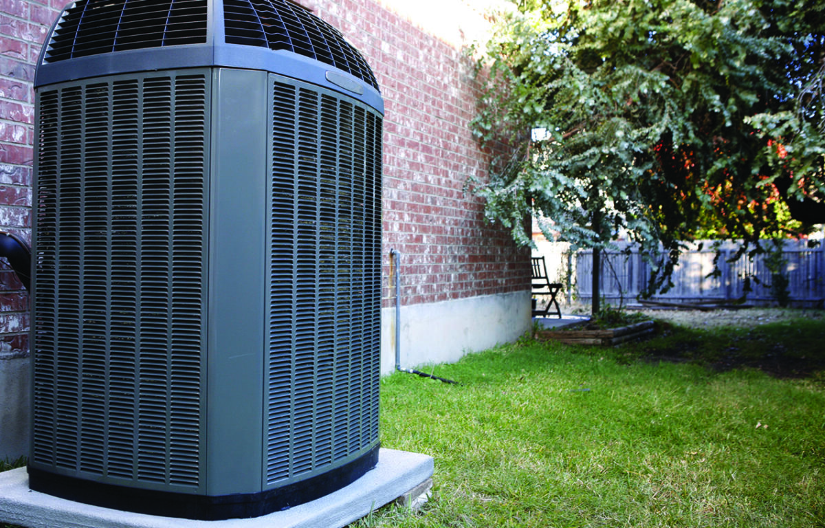 Outdoor air conditioner condenser unit on a concrete pad beside a brick wall and green lawn.