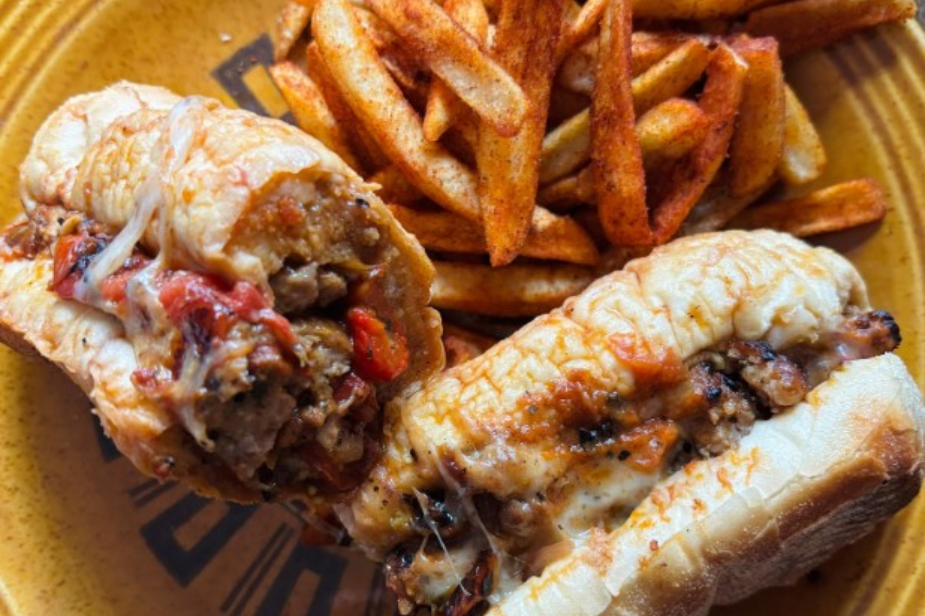 Plate with two stuffed chicken drumsticks with melted cheese and peppers, paired with seasoned French fries on a yellow plate.