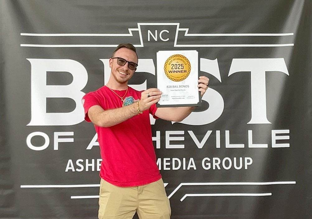 Smiling man in a red shirt holds a 2025 winner plaque in front of a 'Best of Asheville' banner backdrop.
