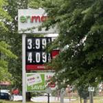 Gas price sign partially obscured by trees, showing prices like 3.99 and 4.09 per litre.
