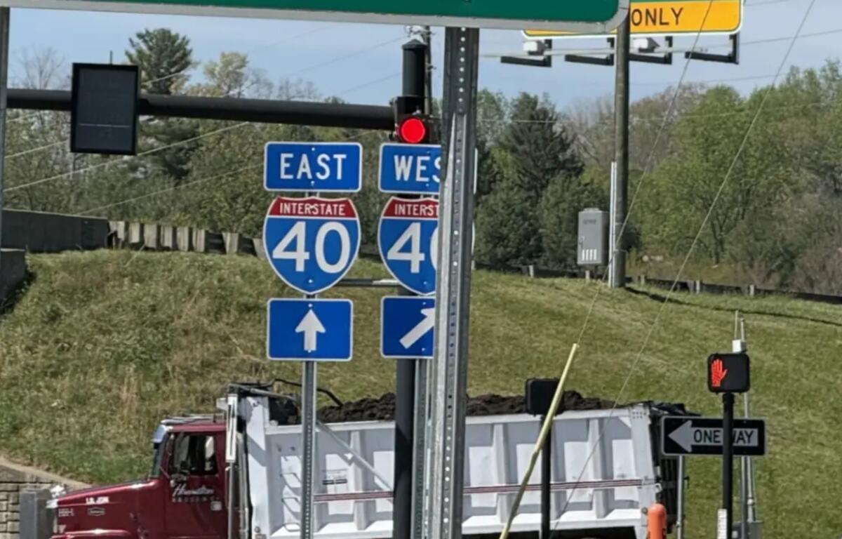 Interstate 40 east and west signs with construction trucks in the background, indicating a highway junction under work.
