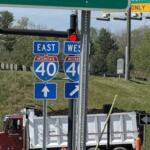 Interstate 40 east and west signs with construction trucks in the background, indicating a highway junction under work.