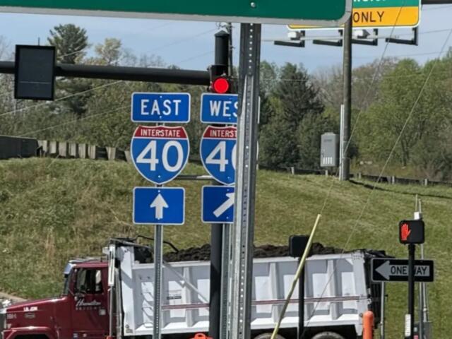 Interstate 40 east and west signs with construction trucks in the background, indicating a highway junction under work.