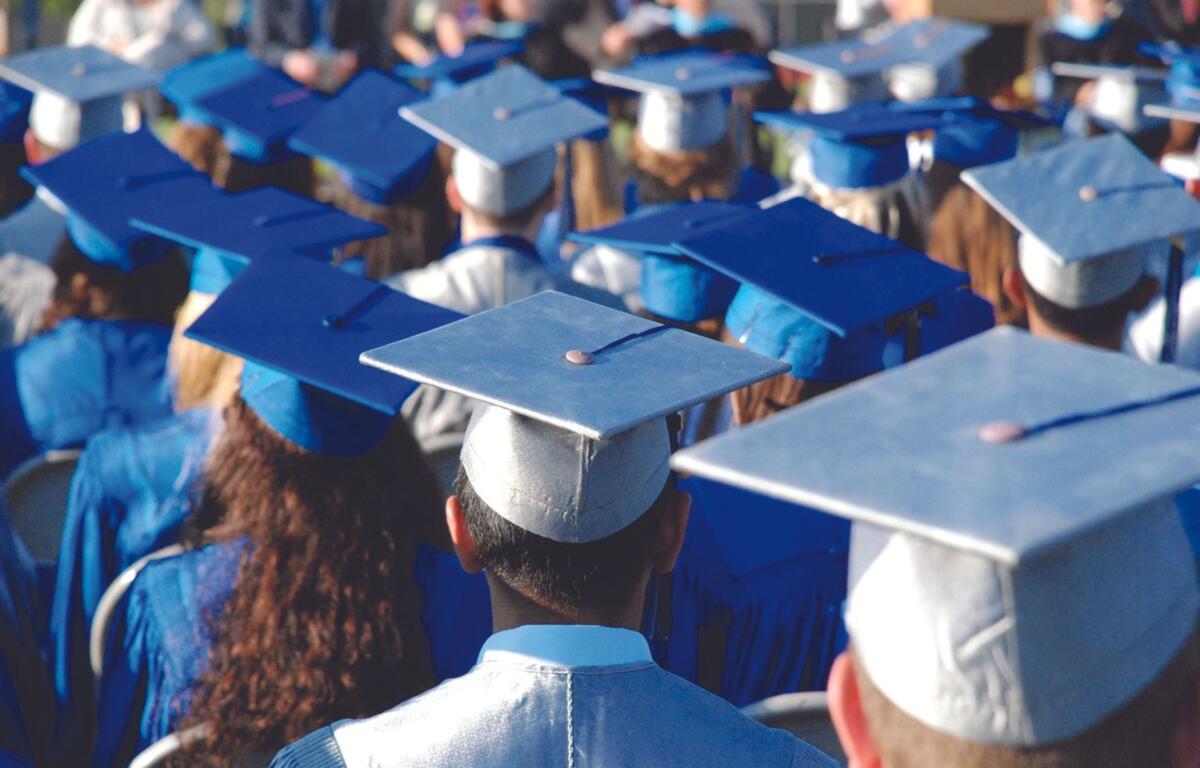Back view of graduates in blue caps and gowns at a commencement ceremony, facing away from the camera.
