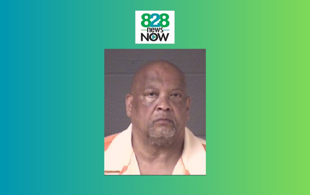 Mugshot portrait of an older man wearing an orange-and-white shirt, set against a gray background with 828 News Now branding above on a teal-green gradient.