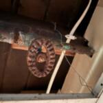 Rusty circular pulley hanging from a pipe in a dusty ceiling space.