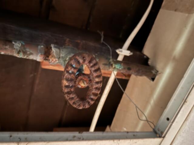 Rusty circular pulley hanging from a pipe in a dusty ceiling space.
