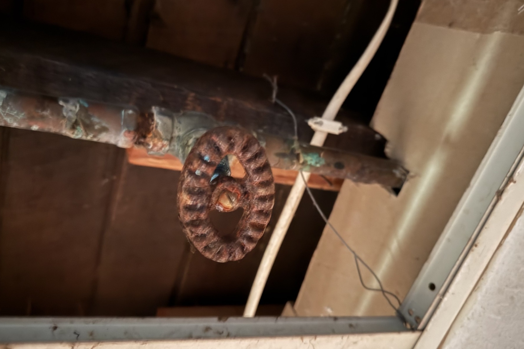 Rusty circular pulley hanging from a pipe in a dusty ceiling space.