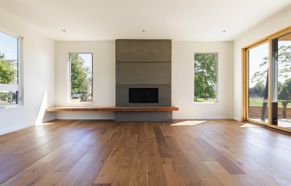 Bright living room with a tall gray paneled fireplace centered on the wall, flanked by two narrow windows and a sliding glass door.