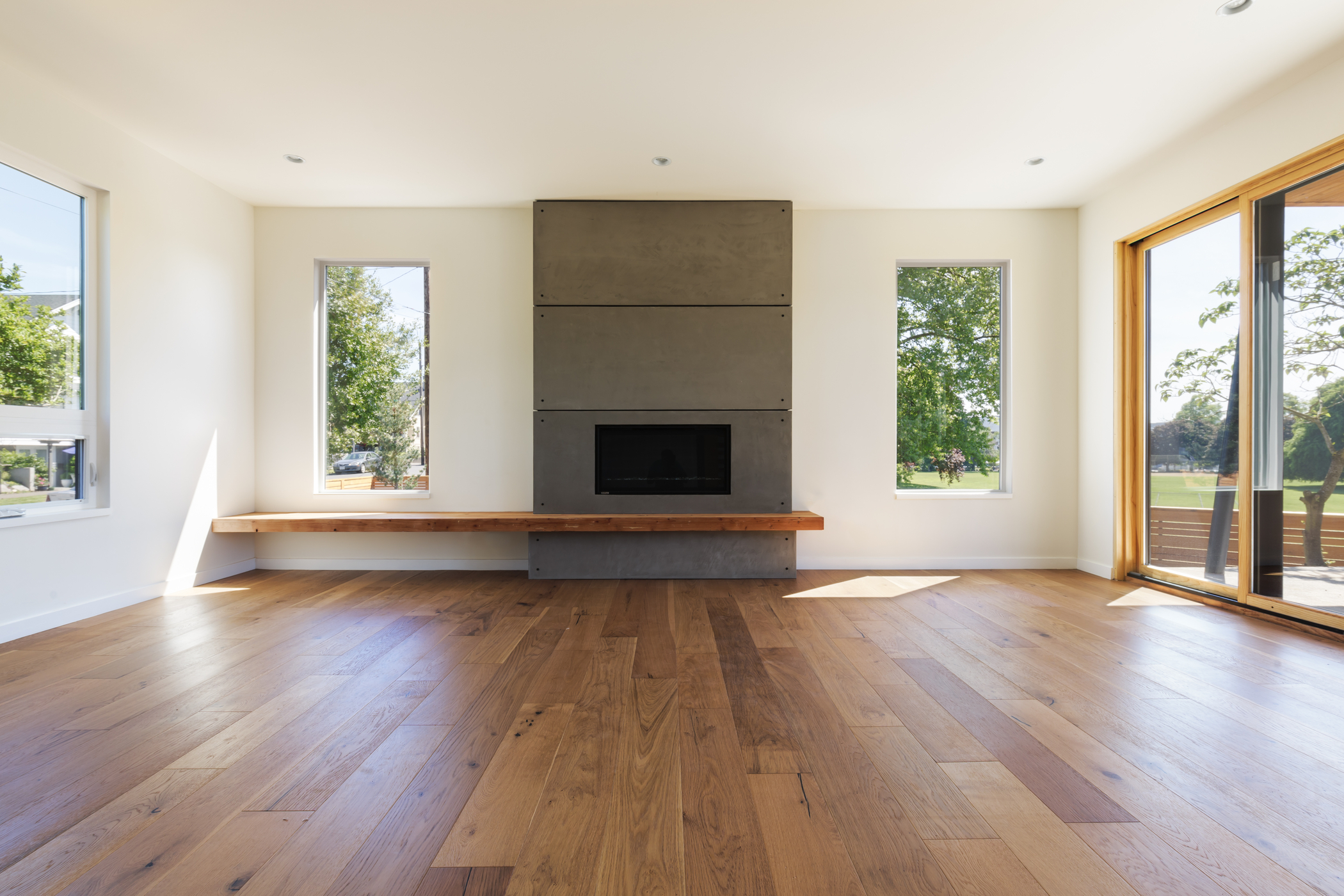 Bright living room with a tall gray paneled fireplace centered on the wall, flanked by two narrow windows and a sliding glass door.