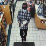 Person wearing a plaid shirt walking down an aisle in a grocery store, shelves stocked with products on the left.