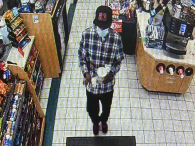 Person wearing a plaid shirt walking down an aisle in a grocery store, shelves stocked with products on the left.