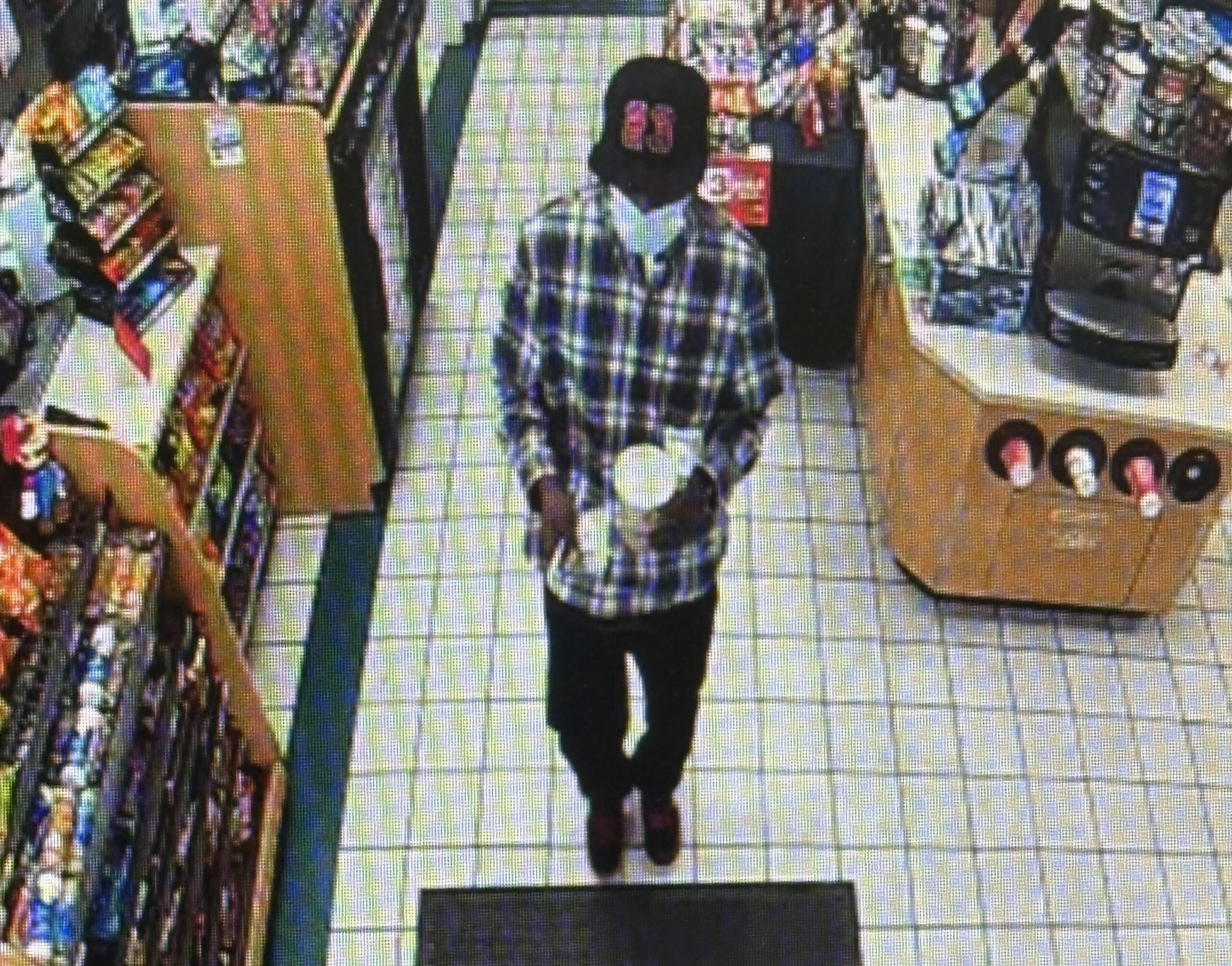 Person wearing a plaid shirt walking down an aisle in a grocery store, shelves stocked with products on the left.