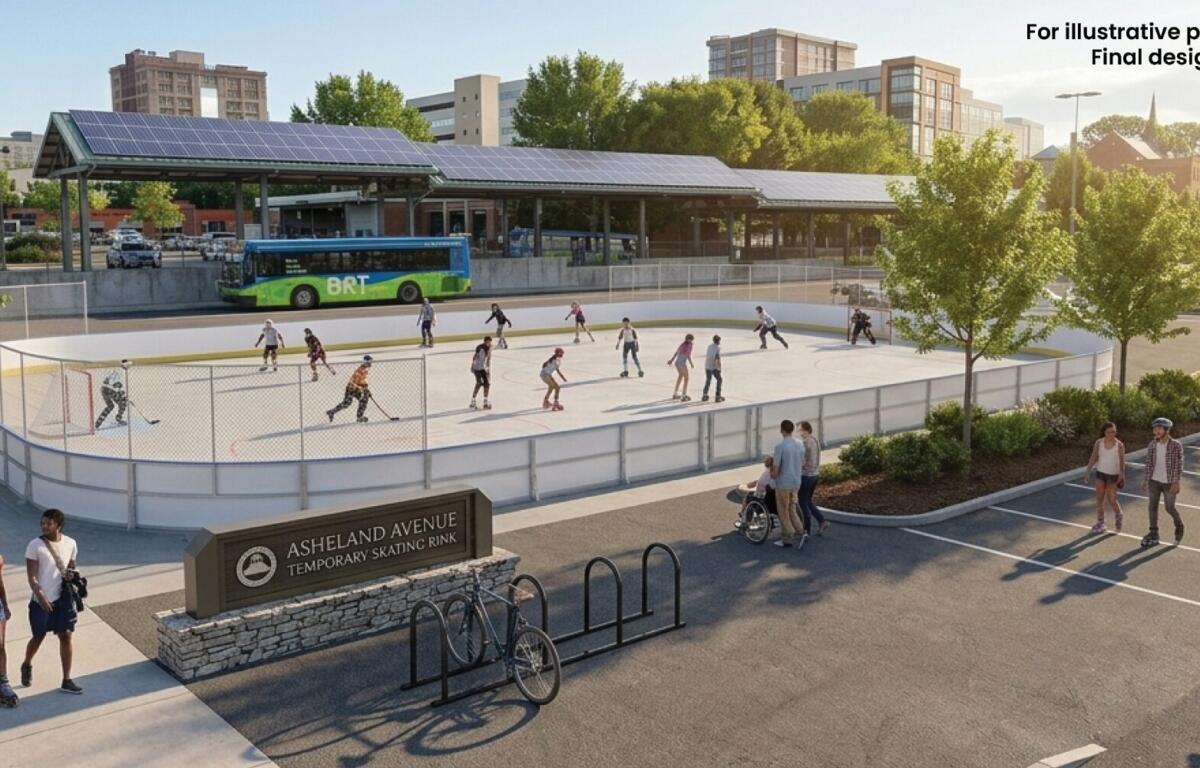 People skate on an outdoor rink surrounded by trees and pedestrians, with a city bus and buildings in the background.