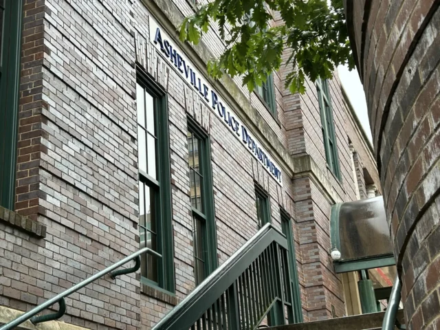Brick building exterior with green-framed windows and an exterior metal stair railing along a narrow alley. (Informative)
