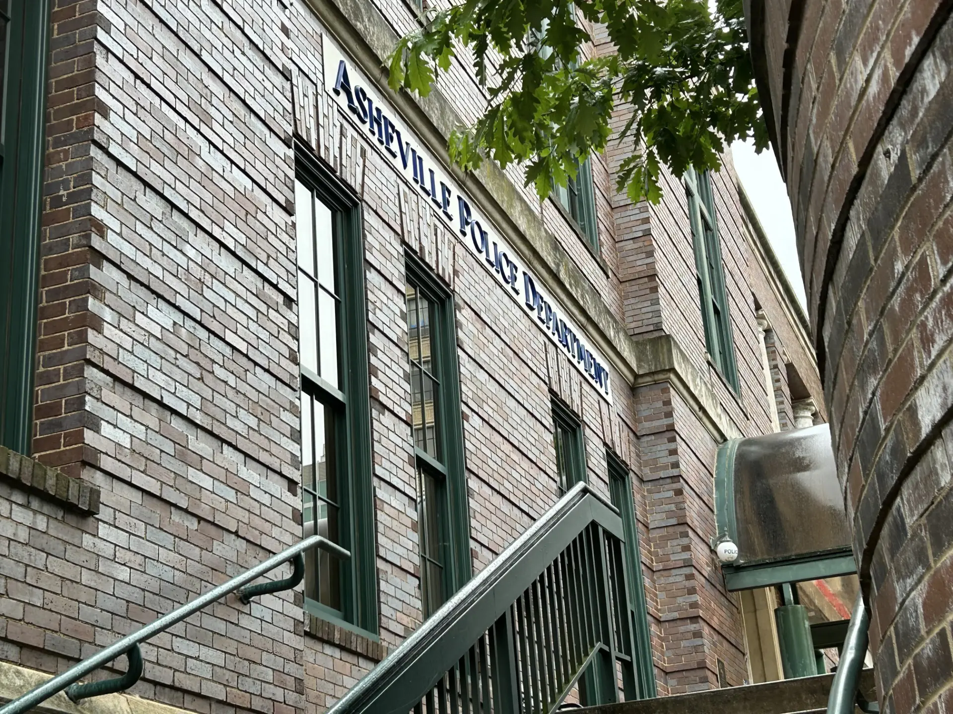 Brick building exterior with green-framed windows and an exterior metal stair railing along a narrow alley. (Informative)