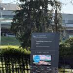 VA sign for the U.S. Department of Veterans Affairs with Charles George VA Medical Center, Asheville, visible beside a fence and greenery.