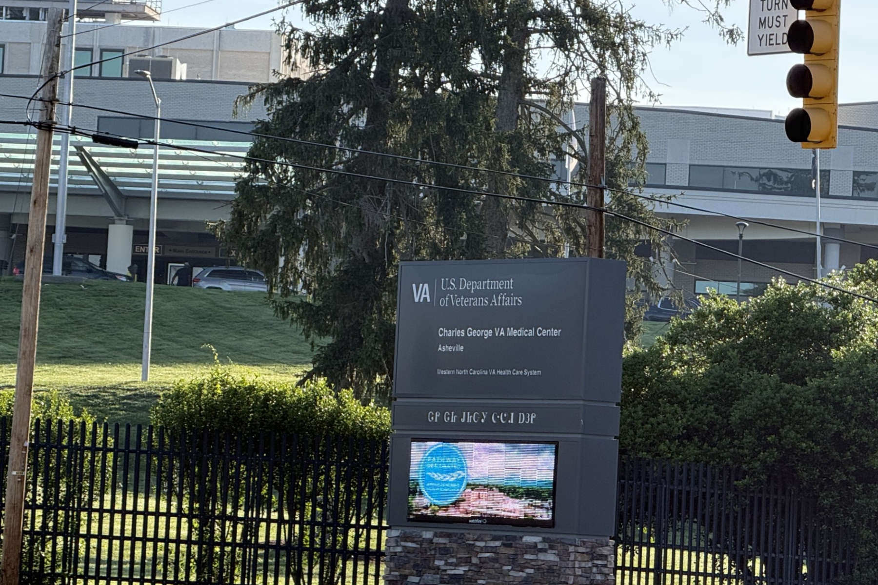 VA sign for the U.S. Department of Veterans Affairs with Charles George VA Medical Center, Asheville, visible beside a fence and greenery.