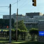 View of a VA Medical Center campus with a street, traffic light, power lines, and a prominent hospital sign at the entrance.