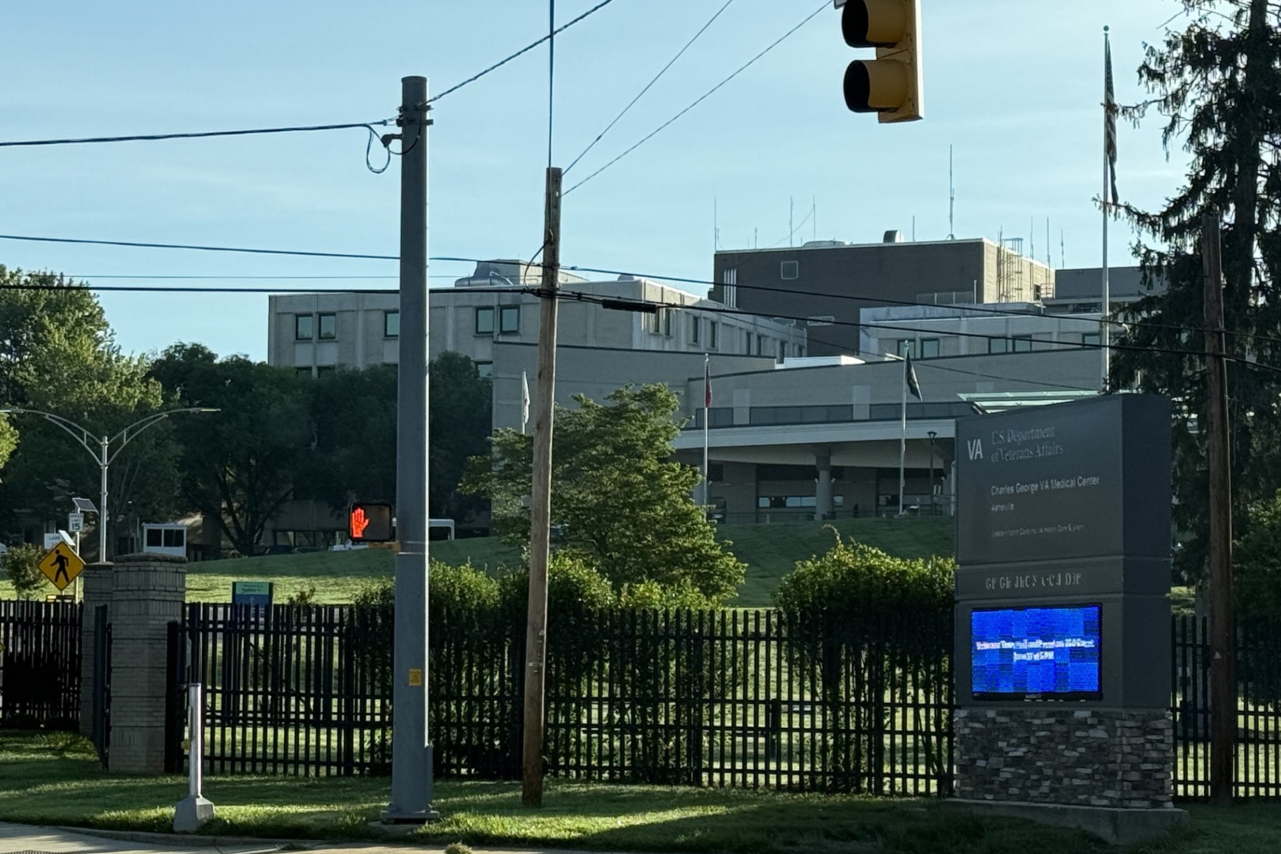 View of a VA Medical Center campus with a street, traffic light, power lines, and a prominent hospital sign at the entrance.