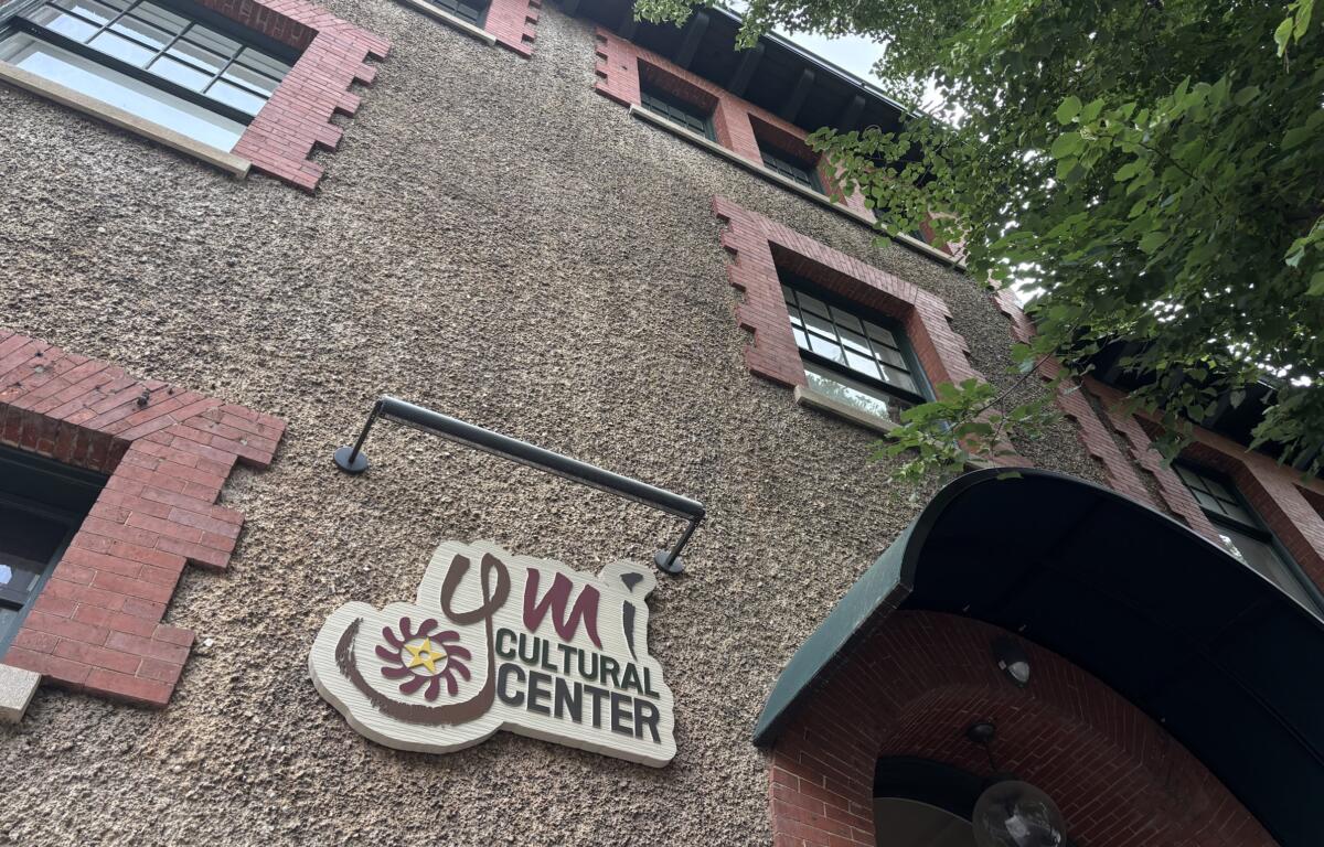 Exterior of a textured beige pebble-dash building with red brick window trim and a Cultural Center sign, with leafy branches on the right.