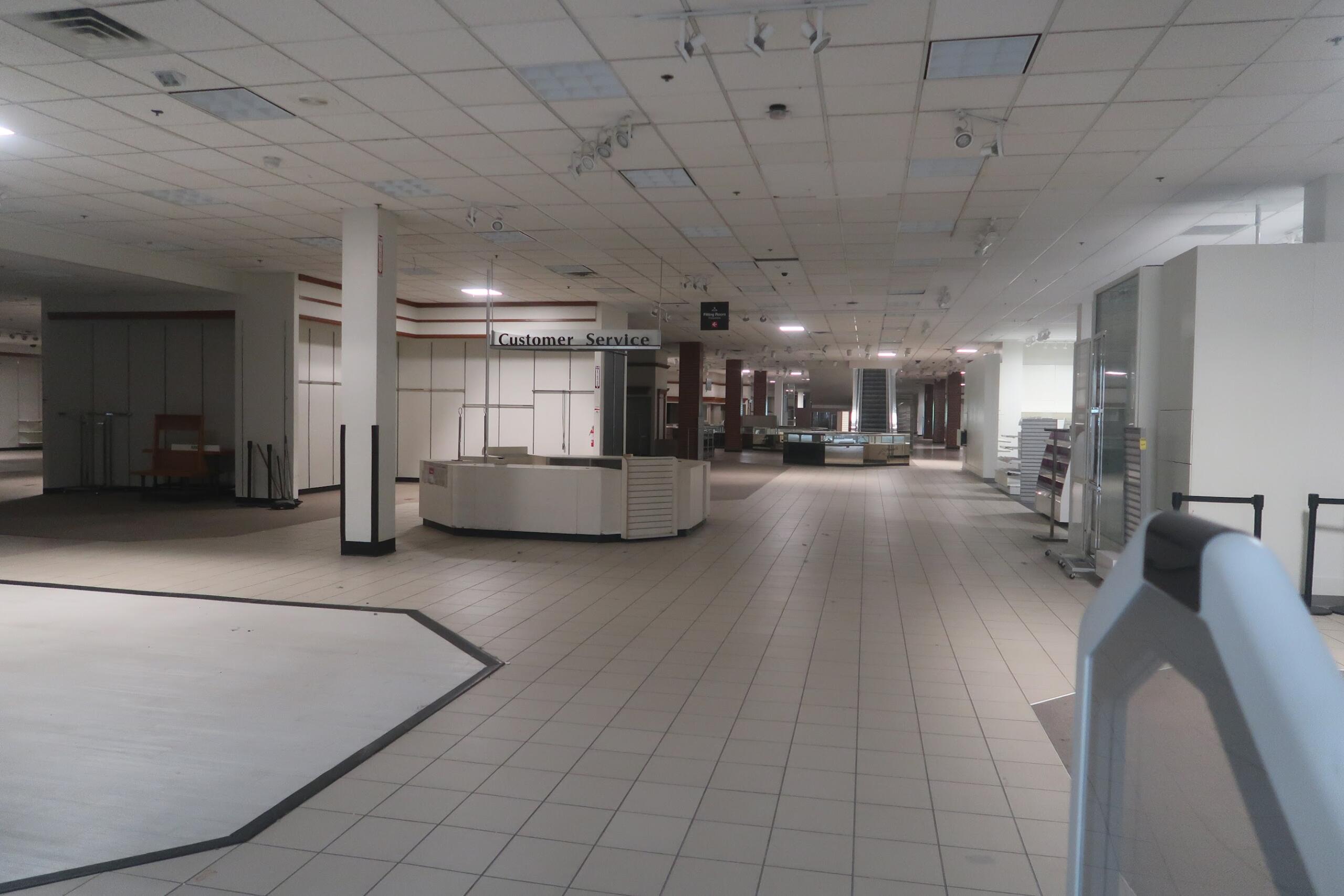 Empty department store interior with a curved white service counter and a 'Customer Service' sign in the distance.