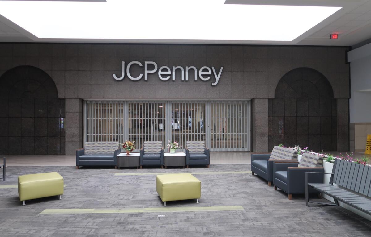 Seating lounge in a mall in front of a JC Penney storefront with gray couches and small tables with flowers.