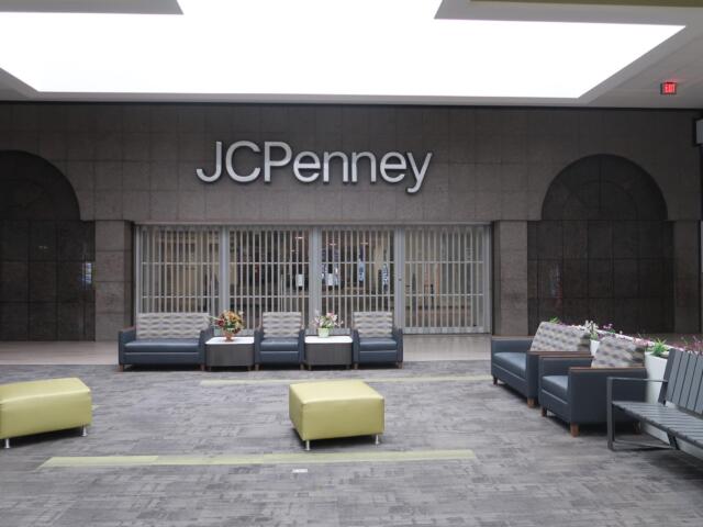 Seating lounge in a mall in front of a JC Penney storefront with gray couches and small tables with flowers.